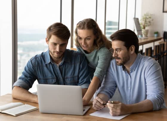 Three co-workers looking at a laptop